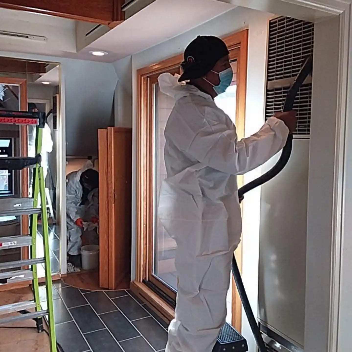 Technician in a protective suit vacuuming the trim around a window